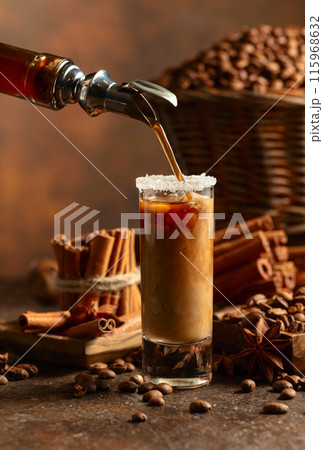 Coffee liqueur is poured from a bottle into a glass with cream. 115968632