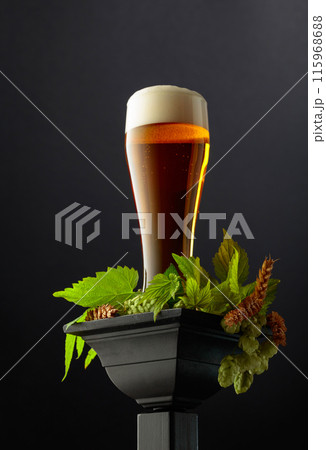 Beer with green hops and wheat ears on a black podium. 115968688