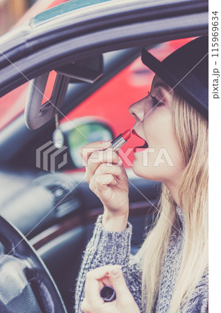 Young woman applying lipstick in car 115969634