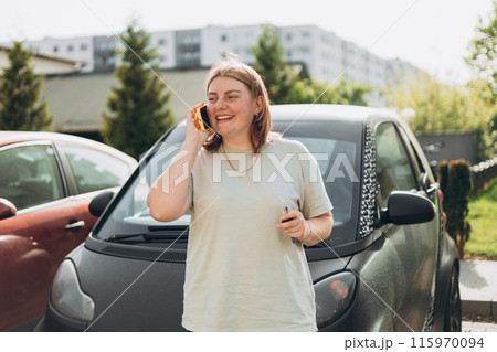 Smiling woman standing near her automobile on a parking and having a phone conversation. Urban lifestyle, technology concept. Smiling woman standing near her automobile on a parking and having a phone conversation. Urban lifestyle, technology concept. 115970094