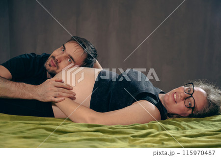 A pregnant woman lies on a green blanket, her man's head touching her belly. A family awaiting the birth of a baby. Family. Husband's care for his wife. 115970487