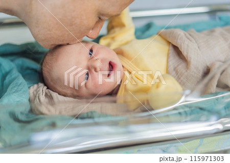 Mom kisses her newborn baby who is resting in a transparent cradle in the hospital. This tender moment emphasizes the bond between mother and child, creating a cozy and safe atmosphere for the infant Mom kisses her newborn baby who is resting in a transparent cradle in the hospital. This tender moment emphasizes the bond between mother and child, creating a cozy and safe atmosphere for the infant 115971303
