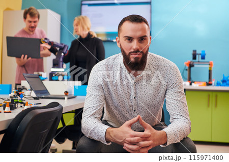 A man sitting in a robotics laboratory while his colleagues in the background test new, cutting edge robotic inventions. A man sitting in a robotics laboratory while his colleagues in the background test new, cutting edge robotic inventions. 115971400