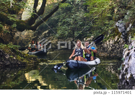 A group of friends enjoying having fun and kayaking while exploring the calm river, surrounding forest and large natural river canyons A group of friends enjoying having fun and kayaking while exploring the calm river, surrounding forest and large natural river canyons 115971401