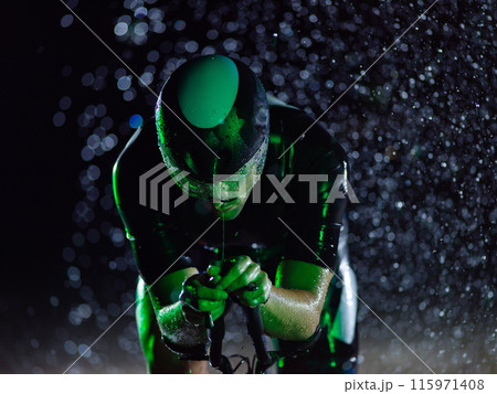 A triathlete braving the rain as he cycles through the night, preparing himself for the upcoming marathon. The blurred raindrops in the foreground and the dark, moody atmosphere in the background add A triathlete braving the rain as he cycles through the night, preparing himself for the upcoming marathon. The blurred raindrops in the foreground and the dark, moody atmosphere in the background add 115971408