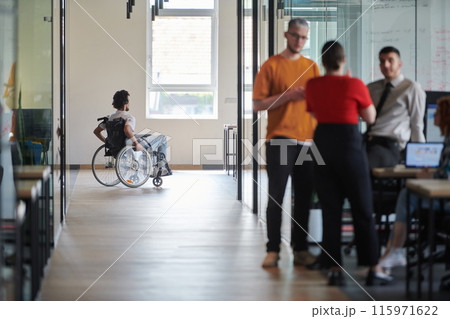 A diverse group of colleagues engages in a discussion about business challenges within a modern coworking startup center, while in the background, their wheelchair-bound colleague symbolizes A diverse group of colleagues engages in a discussion about business challenges within a modern coworking startup center, while in the background, their wheelchair-bound colleague symbolizes 115971622