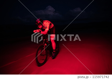 A triathlete rides his bike in the darkness of night, pushing himself to prepare for a marathon. The contrast between the darkness and the light of his bike creates a sense of drama and highlights the 115971742