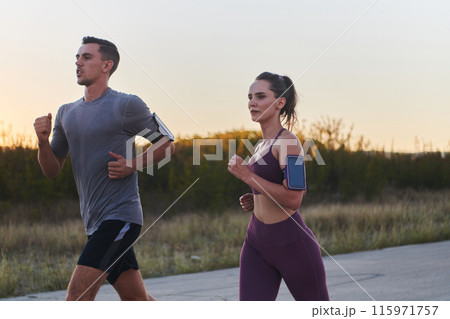 A handsome young couple running together during the early morning hours, with the mesmerizing sunrise casting a warm glow, symbolizing their shared love and vitality 115971757