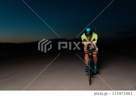 A triathlete rides his bike in the darkness of night, pushing himself to prepare for a marathon. The contrast between the darkness and the light of his bike creates a sense of drama and highlights the A triathlete rides his bike in the darkness of night, pushing himself to prepare for a marathon. The contrast between the darkness and the light of his bike creates a sense of drama and highlights the 115971861