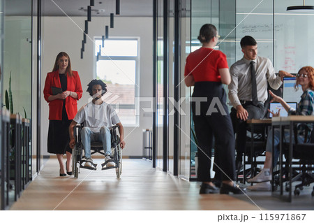 A group of young business people in a modern glass-walled office captures the essence of diversity and collaboration, while two colleagues, including an African American businessman in a wheelchair 115971867