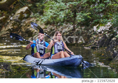 A young couple enjoying an idyllic kayak ride in the middle of a beautiful river surrounded by forest greenery 115972020