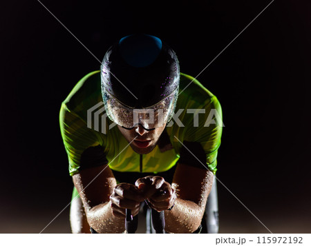 A triathlete rides his bike in the darkness of night, pushing himself to prepare for a marathon. The contrast between the darkness and the light of his bike creates a sense of drama and highlights the 115972192