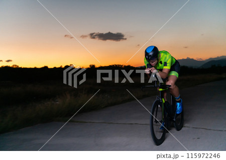 A triathlete rides his bike in the darkness of night, pushing himself to prepare for a marathon. The contrast between the darkness and the light of his bike creates a sense of drama and highlights the 115972246