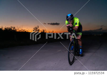 A triathlete rides his bike in the darkness of night, pushing himself to prepare for a marathon. The contrast between the darkness and the light of his bike creates a sense of drama and highlights the A triathlete rides his bike in the darkness of night, pushing himself to prepare for a marathon. The contrast between the darkness and the light of his bike creates a sense of drama and highlights the 115972534