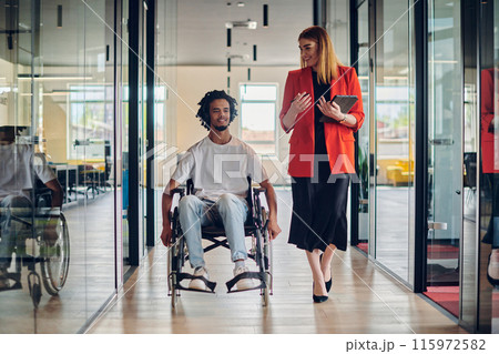 A group of young business people in a modern glass-walled office captures the essence of diversity and collaboration, while two colleagues, including an African American businessman in a wheelchair A group of young business people in a modern glass-walled office captures the essence of diversity and collaboration, while two colleagues, including an African American businessman in a wheelchair 115972582