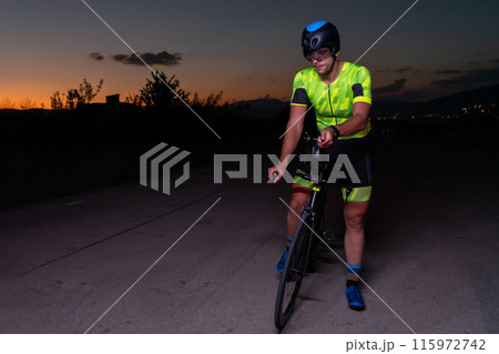 A triathlete rides his bike in the darkness of night, pushing himself to prepare for a marathon. The contrast between the darkness and the light of his bike creates a sense of drama and highlights the 115972742