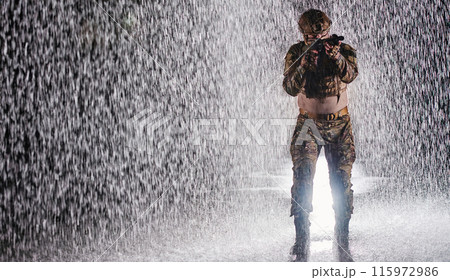 Army soldier in Combat Uniforms with an assault rifle, plate carrier and combat helmet going on a dangerous mission on a rainy night. 115972986