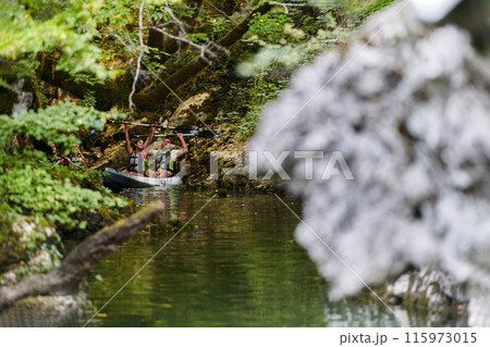 A young couple enjoying an idyllic kayak ride in the middle of a beautiful river surrounded by forest greenery 115973015