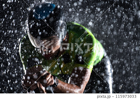 A triathlete braving the rain as he cycles through the night, preparing himself for the upcoming marathon. The blurred raindrops in the foreground and the dark, moody atmosphere in the background add A triathlete braving the rain as he cycles through the night, preparing himself for the upcoming marathon. The blurred raindrops in the foreground and the dark, moody atmosphere in the background add 115973033