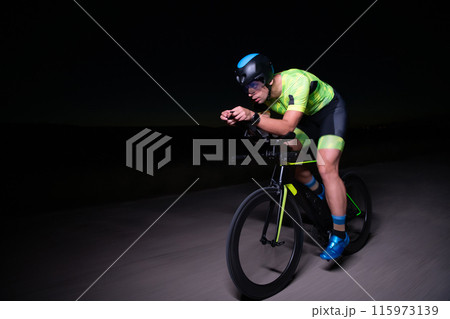A triathlete rides his bike in the darkness of night, pushing himself to prepare for a marathon. The contrast between the darkness and the light of his bike creates a sense of drama and highlights the 115973139