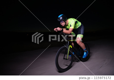 A triathlete rides his bike in the darkness of night, pushing himself to prepare for a marathon. The contrast between the darkness and the light of his bike creates a sense of drama and highlights the 115973172