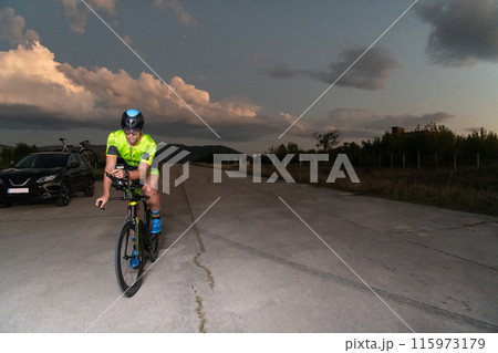 A triathlete rides his bike in the darkness of night, pushing himself to prepare for a marathon. The contrast between the darkness and the light of his bike creates a sense of drama and highlights the 115973179