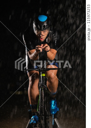 A triathlete braving the rain as he cycles through the night, preparing himself for the upcoming marathon A triathlete braving the rain as he cycles through the night, preparing himself for the upcoming marathon 115973253