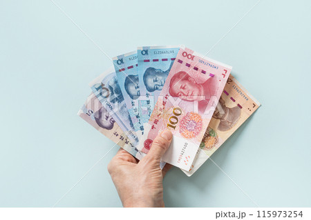Many of different Chinese yuan banknotes in female hand. Chinese paper currency Yuan renminbi banknotes and coins on blue background. Copy space. 115973254
