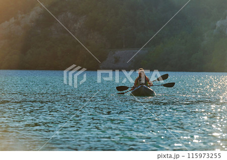 A young couple enjoying an idyllic kayak ride in the middle of a beautiful river surrounded by forest greenery in sunset time A young couple enjoying an idyllic kayak ride in the middle of a beautiful river surrounded by forest greenery in sunset time 115973255