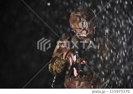 Army soldier in Combat Uniforms with an assault rifle, plate carrier and combat helmet going on a dangerous mission on a rainy night. Army soldier in Combat Uniforms with an assault rifle, plate carrier and combat helmet going on a dangerous mission on a rainy night. 115973370
