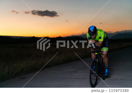 A triathlete rides his bike in the darkness of night, pushing himself to prepare for a marathon. The contrast between the darkness and the light of his bike creates a sense of drama and highlights the A triathlete rides his bike in the darkness of night, pushing himself to prepare for a marathon. The contrast between the darkness and the light of his bike creates a sense of drama and highlights the 115973380