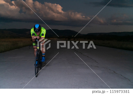 A triathlete rides his bike in the darkness of night, pushing himself to prepare for a marathon. The contrast between the darkness and the light of his bike creates a sense of drama and highlights the A triathlete rides his bike in the darkness of night, pushing himself to prepare for a marathon. The contrast between the darkness and the light of his bike creates a sense of drama and highlights the 115973381