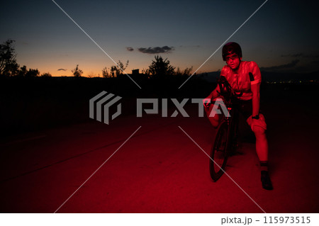 A triathlete resting on the road after a tough bike ride in the dark night, leaning on his bike in complete exhaustion A triathlete resting on the road after a tough bike ride in the dark night, leaning on his bike in complete exhaustion 115973515