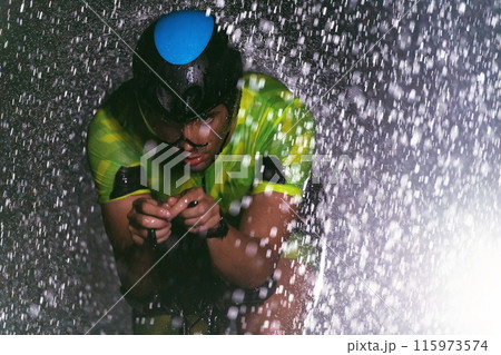 A triathlete braving the rain as he cycles through the night, preparing himself for the upcoming marathon A triathlete braving the rain as he cycles through the night, preparing himself for the upcoming marathon 115973574