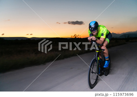 A triathlete rides his bike in the darkness of night, pushing himself to prepare for a marathon. The contrast between the darkness and the light of his bike creates a sense of drama and highlights the 115973696