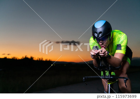 A triathlete rides his bike in the darkness of night, pushing himself to prepare for a marathon. The contrast between the darkness and the light of his bike creates a sense of drama and highlights the A triathlete rides his bike in the darkness of night, pushing himself to prepare for a marathon. The contrast between the darkness and the light of his bike creates a sense of drama and highlights the 115973699