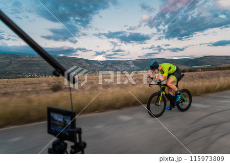 A videographer recording a triathlete riding his bike preparing for an upcoming marathon.Athlete's physical endurance and the dedication required to succeed in the sport. 115973809