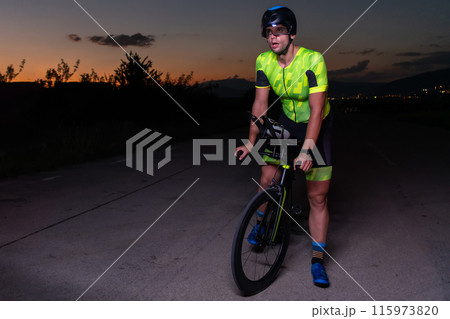 A triathlete rides his bike in the darkness of night, pushing himself to prepare for a marathon. The contrast between the darkness and the light of his bike creates a sense of drama and highlights the 115973820