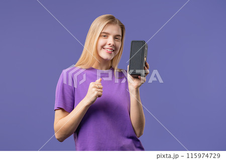 Blonde woman listening music by wireless portable speaker - sound system, violet 115974729