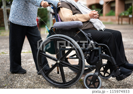 Elderly woman in wheel chair spending time with her daughter in the garden of nursing home 115974933
