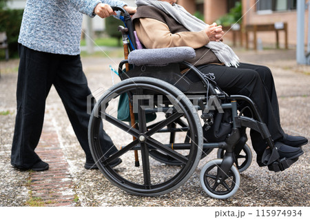 Elderly woman in wheel chair spending time with her daughter in the garden of nursing home 115974934