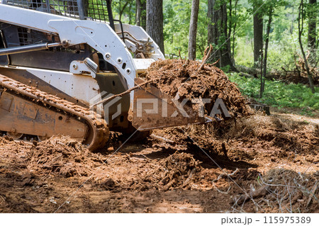 At forest, tractor is using bucket to level ground during earthworks At forest, tractor is using bucket to level ground during earthworks 115975389