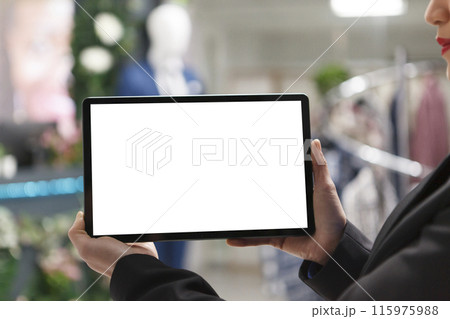 Woman hands holding digital tablet empty white touchscreen mockup closeup in clothing store. Shopping department mall consultant using portable gadget with blank screen for app 115975988