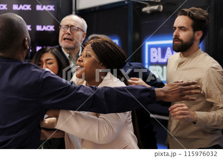 People shoppers going crazy to get to store first in order to get best deals during Black Friday sales. Angry crowd of customers fighting with security officer while waiting at shopping mall entrance 115976032