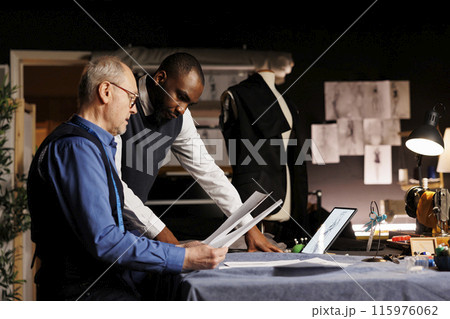 Tailors checking fashion sketch designs, trying different attire combinations on mannequin in haute couture atelier. Master craftsman and apprentice working on bespoke suit alterations Tailors checking fashion sketch designs, trying different attire combinations on mannequin in haute couture atelier. Master craftsman and apprentice working on bespoke suit alterations 115976062
