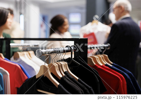 Seasonal shopping. Close up of different branded clothes hanging on garment rack in fashion outlet, people doing purchases in clothing store during clearance sales. Retail business concept Seasonal shopping. Close up of different branded clothes hanging on garment rack in fashion outlet, people doing purchases in clothing store during clearance sales. Retail business concept 115976225