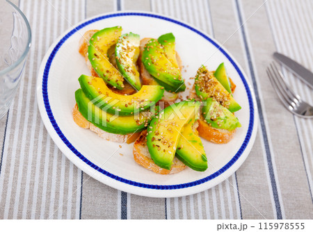 On plate are sandwiches with bran bread and avocado, sprinkled with sesame seeds On plate are sandwiches with bran bread and avocado, sprinkled with sesame seeds 115978555