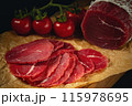 Whole and sliced bresaola on paper on a cutting board with tomatoes 115978695