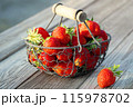 Fresh ripe strawberries in a metal basket on an outdoor wooden table 115978702