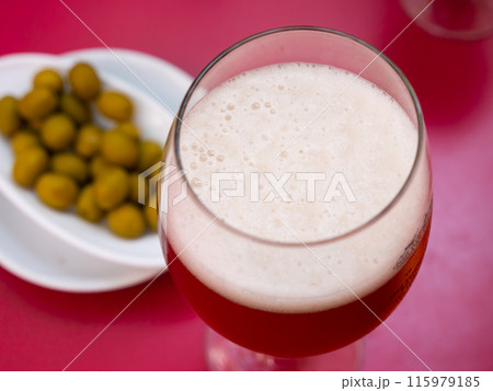 Glass of foamy chilled beer with green pickled olives 115979185